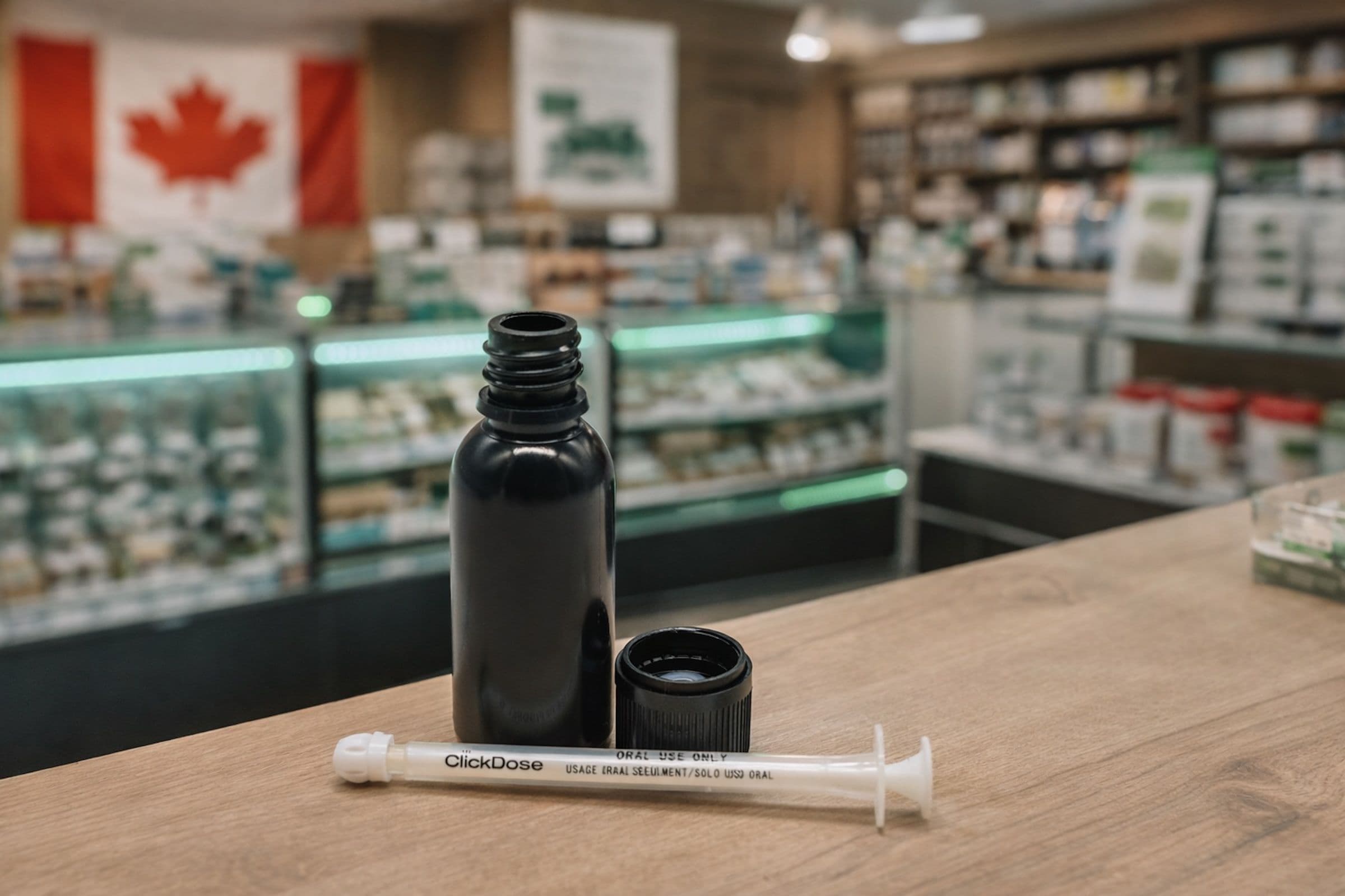 Black 30 mL plastic bottle with cap and oral dosing syringe displayed on a counter in a Canadian cannabis retail store setting